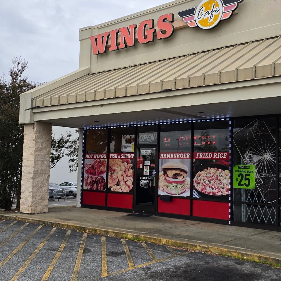 Exterior of Wings Cafe restaurant with menu images of hot wings, fish, shrimp, hamburger, and fried rice.