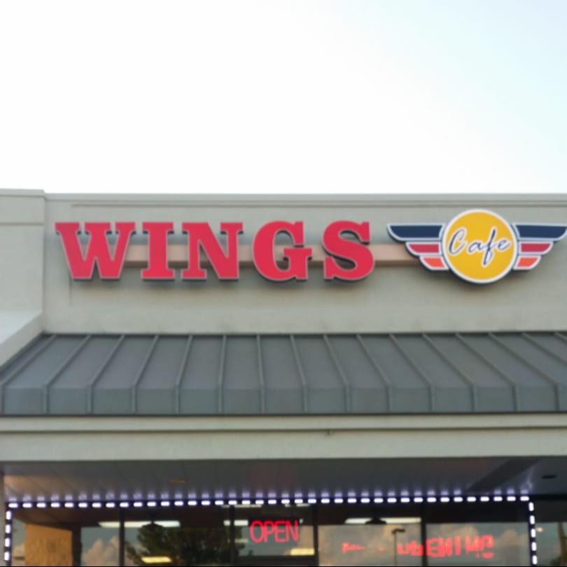 The exterior sign of "Wings Cafe" with red lettering and a winged logo, above an "OPEN" sign.