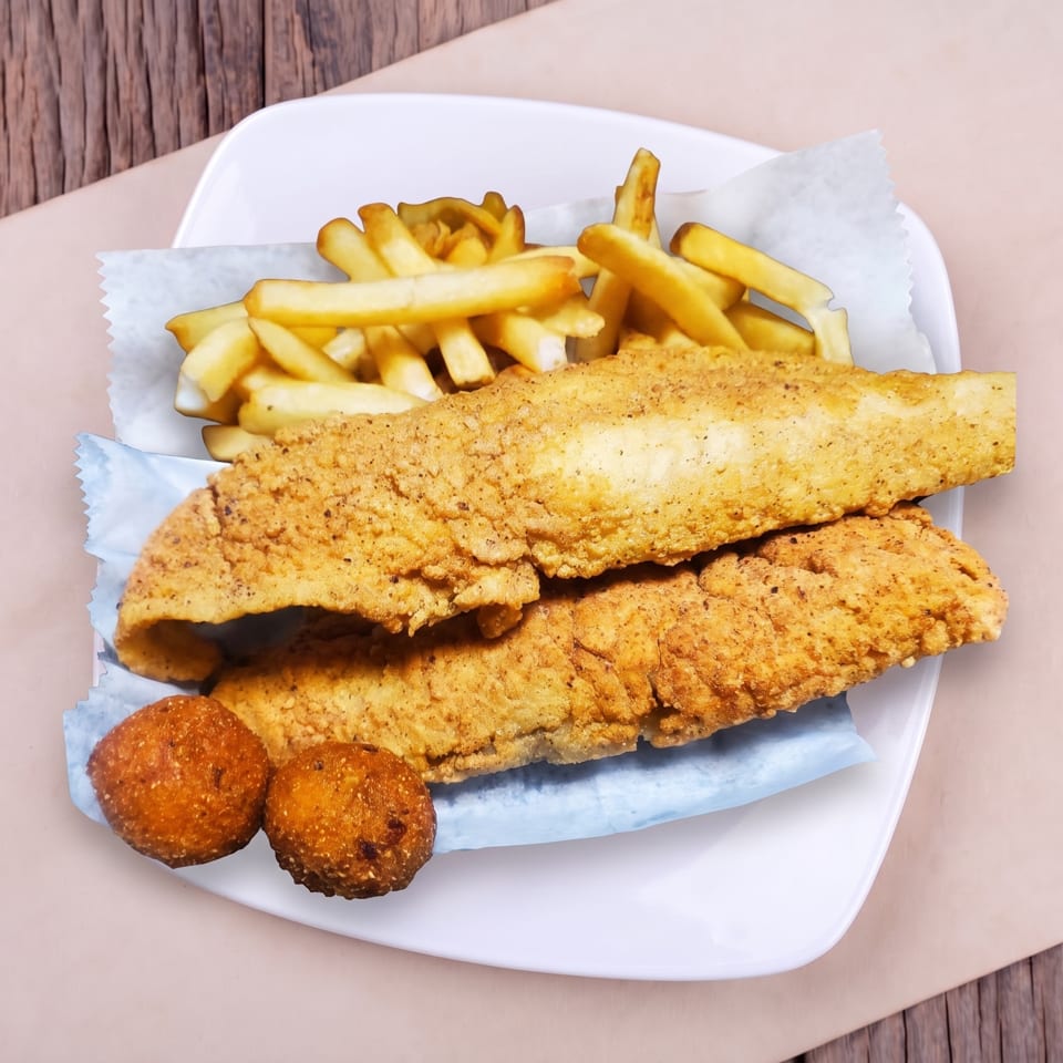 Crispy fried fish fillets, golden french fries, and hush puppies on a white plate.