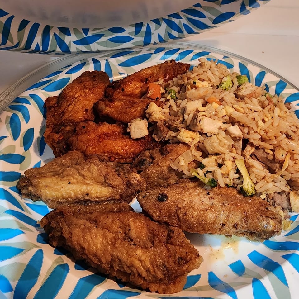 Fried chicken wings and chicken fried rice with vegetables on a blue and white patterned plate.