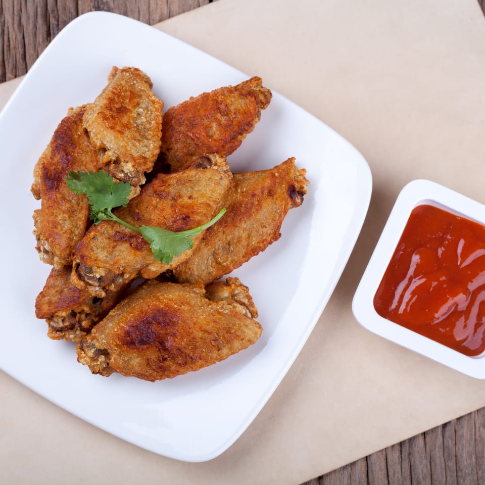 Golden fried chicken wings with cilantro on a white plate, next to red dipping sauce.