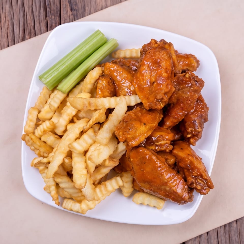 Appetizer plate with buffalo chicken wings, crinkle-cut fries, and fresh celery sticks.