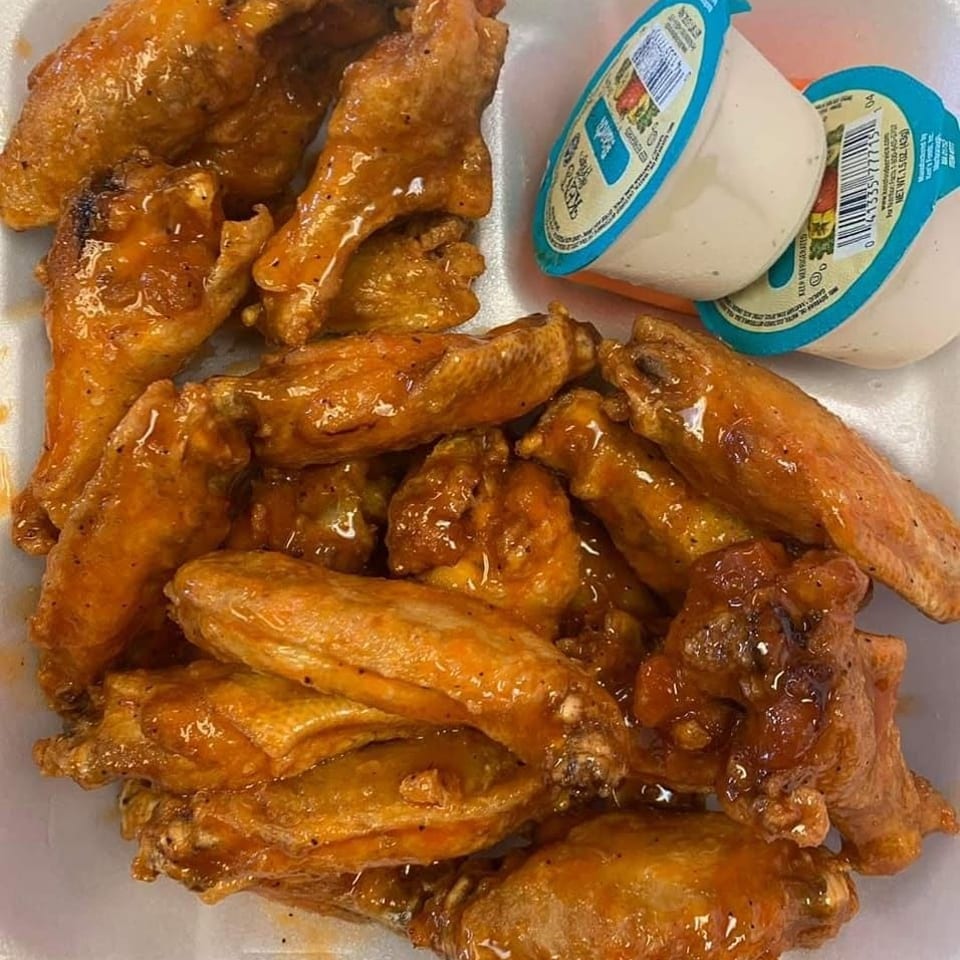 Many glazed chicken wings in a container with two ranch dressing cups.
