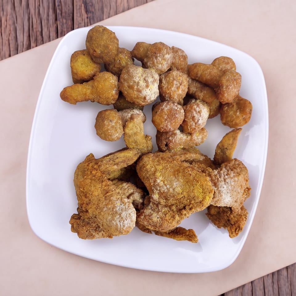 White plate of crispy fried chicken wings and nuggets on a rustic wooden table.
