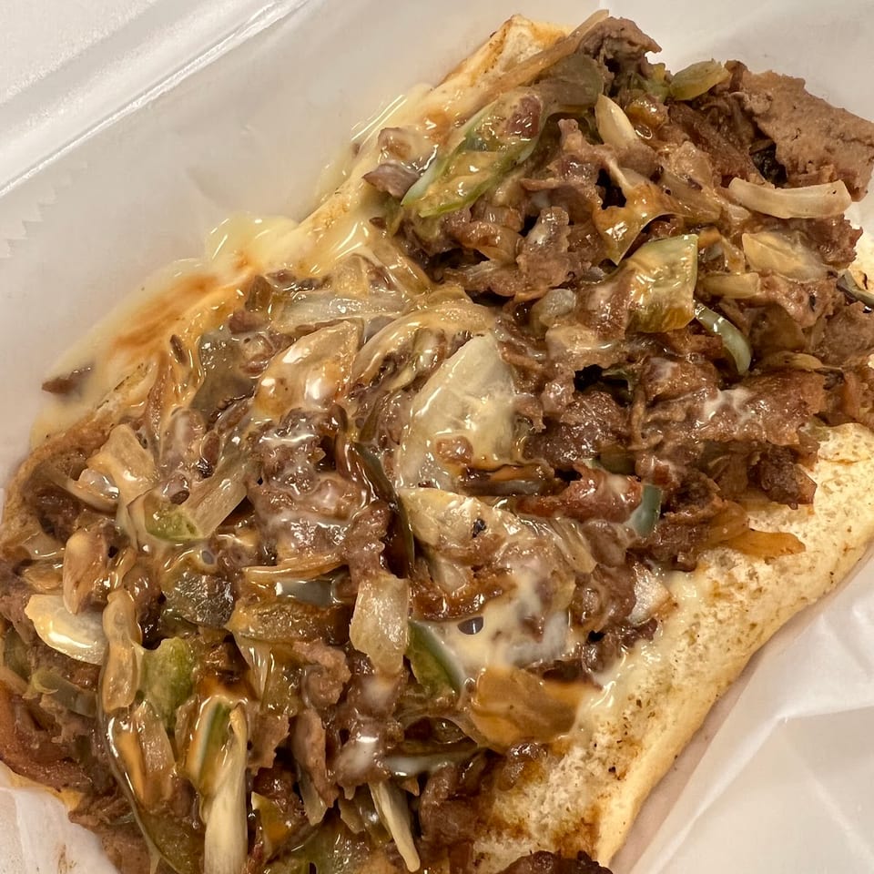 Cheesesteak sandwich with steak, melted cheese, onions, and green peppers in a white container.